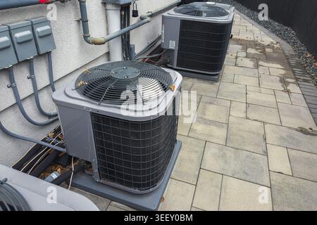 Modern residential air conditioning condenser units installed beside a house with paved walkway and visible utility connections. Stock Photo