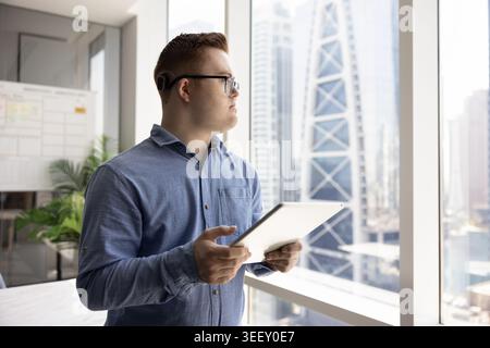 Thoughtful man with Down syndrome working on tablet in office Stock Photo