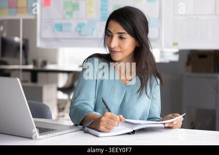 Focused woman taking notes during online meeting Stock Photo