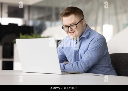 Smiling male office manager with Down syndrome working on laptop Stock Photo
