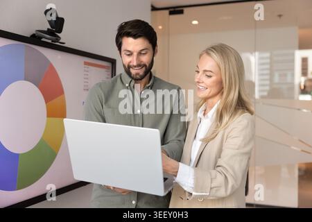Smiling Caucasian male and female colleagues discussing data on laptop Stock Photo