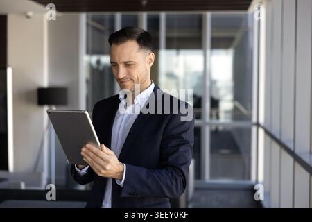 Focused businessman stands in office hallway with tablet Stock Photo