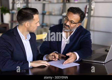 Middle-age consultant explaining details of business document to male client Stock Photo