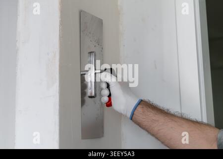 Technician smoothing finishing coat on wall using a stainless steel trowel during renovation work. Clean workspace with minimal clutter and bright lighting enhances detail visibility. Stock Photo