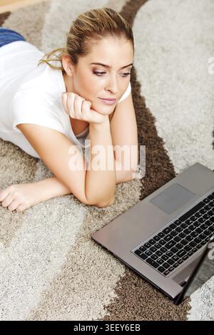 Focused young woman using laptop while lying on floor Stock Photo