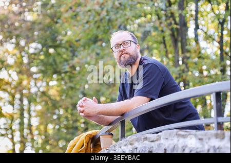 Relaxed individual gazing at nature peacefully. Tranquil man with beard observing treetops from stone bridge calmly. Gentleman with beard takes in peaceful view from stone bridge quietly Stock Photo