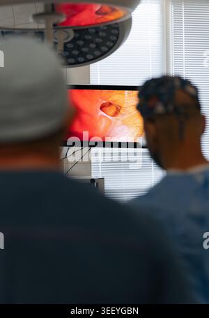 Medical specialists in operating room observing internal view of hernia defect on monitor during laparoscopic surgery. Professional doctors conducting Stock Photo