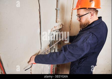 Worker measuring distance along wall pipes with tape. Planning plumbing layout and positioning of utilities during renovation, accuracy and interior construction concept Stock Photo