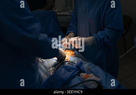Two professional surgeons in blue sterile gowns and masks working together on patient abdomen. Medical specialists using laparoscopic tools and surgic Stock Photo