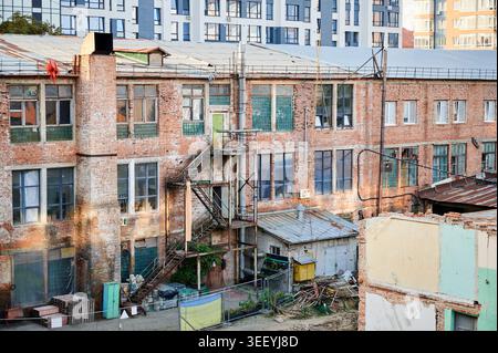 Old industrial brick building with exterior metal stairs and weathered facade in urban area. Suitable for architecture, redevelopment, renovation, and industrial heritage concepts Stock Photo