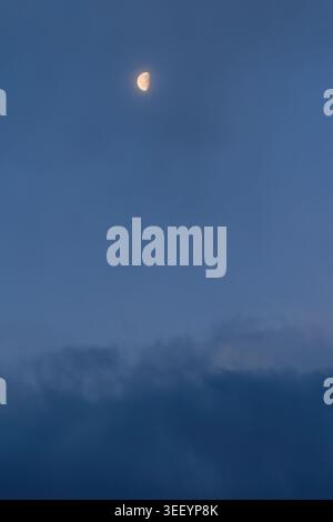 Half Moon in a Clear Blue Evening Sky with Soft Clouds Stock Photo