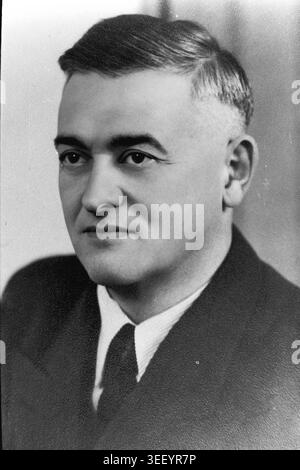 Slavyansk, 1940s, Armature-Insulator Plant named after Artem (AIZ). A formal studio portrait of a man, likely a prominent factory engineer or management representative. He is dressed in a classic dark suit with a white shirt and tie, looking away from the camera with a serious, focused expression. This high-contrast archival photograph preserves the individual human element and personal dedication behind the heavy industrial achievements, reflecting the resilient character and history of the peaceful Donbas. Stock Photo
