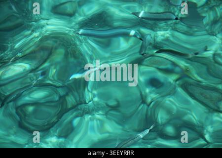 Clear turquoise water ripples gently with sunlight glinting. Smooth patterns shift as waves brush the surface. Cool, calm, and serene, the scene invit Stock Photo