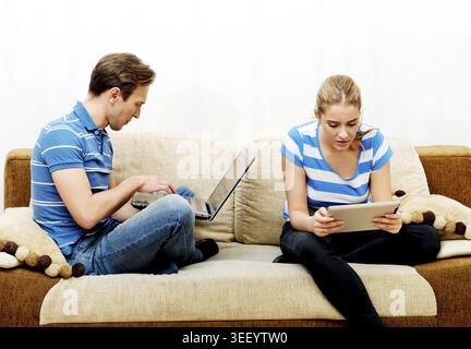 Young couple relaxing on sofa and using tablet and laptop Stock Photo