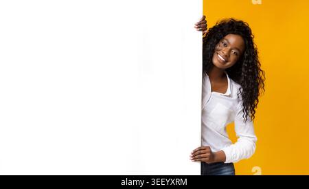Smiling Woman Holding a Blank Canvas on a Bright Yellow Background in a Cheerful Setting Stock Photo