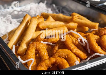 Spring rolls and crispy onion rings, golden fried snacks including with crunchy rice noodles, in a serving tray close-up Stock Photo