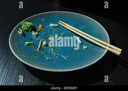 Dirty Sushi Plate on Black Table, Empty Bowl after Sushi Dinner, Finished Asian Lunch, Salad and Wasabi Sauce on Blue Plate Background Top View Stock Photo