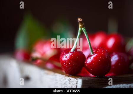 Two cherries on rustic wooden edge, soft bokeh background. Fresh ripe red fruit, natural light food photography Stock Photo