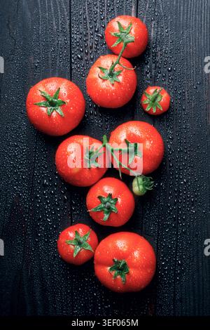 Vertical composition of fresh tomatoes on black surface with water droplets. Healthy vegan food concept Stock Photo