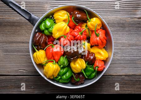 Top view of metal colander filled with habanero peppers on wooden surface. Fresh chili assortment colorful varieties natural food background Stock Photo