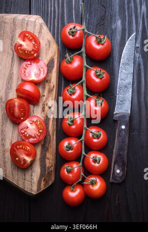Top view of tomatoes on vine with cut halves on wooden board. Fresh natural vegetables, home kitchen styling Stock Photo