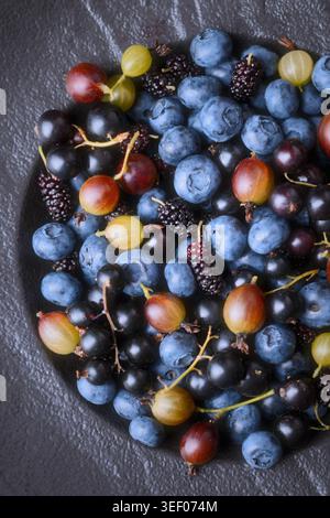 Close up of mixed berries in bowl, vibrant natural colors. Seasonal assortment with blueberries, gooseberries and mixed seasonal fruit Stock Photo