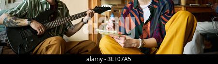 Header of young adults collaborating on songwriting, playing electric guitar, writing lyrics in notebook, expressing creative teamwork. Useful for music production, creative process, artist branding Stock Photo