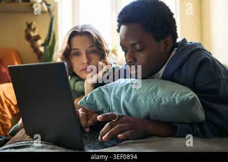 Young Black man and Caucasian woman using laptop together, researching online content at home, showing digital collaboration and shared decision making. For remote learning or tech marketing Stock Photo