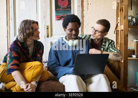 Multiethnic young adults collaborating on laptop while sitting together, discussing project and teamwork. Useful for remote work, startup culture, digital learning, team communication Stock Photo