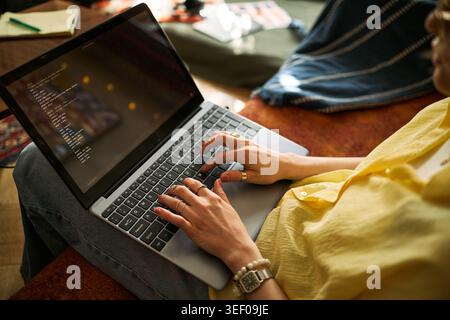 Young adult woman coding on laptop while sitting at home, developing software for remote work and digital business. Useful for programming, freelance tech, startup content Stock Photo