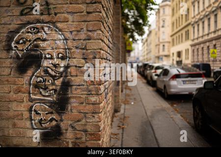 Vienna, Austria - August 4, 2020: Black spray painted silhouettes of grimacing fanged faces and question mark on a yellow brick corner wall along a pa Stock Photo