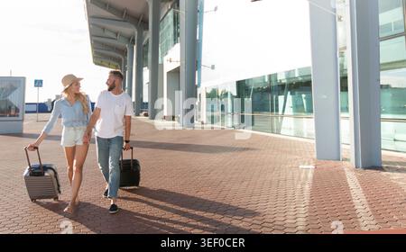 Happy couple walking in front of airport terminal building Stock Photo