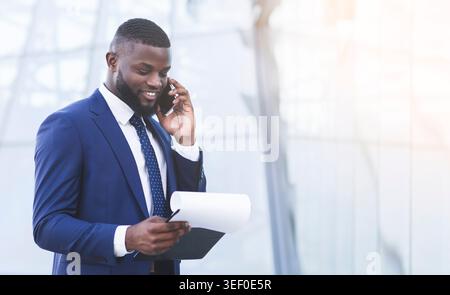 Entrepreneur Talking On Mobile Phone Holding Papers Standing In City Stock Photo