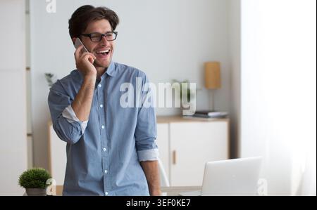 Young Man Enjoys Conversation on Smartphone While Standing in Bright Office Stock Photo