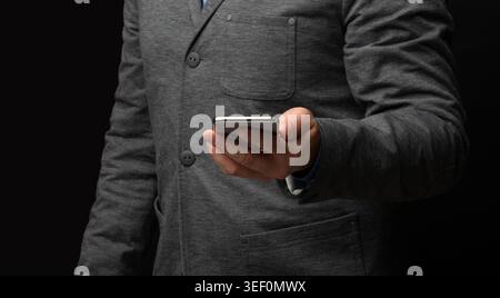 Man in Gray Suit Holding Smartphone Against Dark Background Stock Photo
