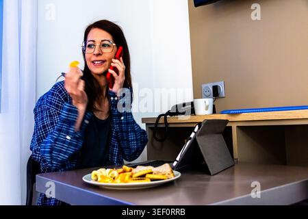 Woman multitasking working remotely having breakfast and talking on phone Stock Photo