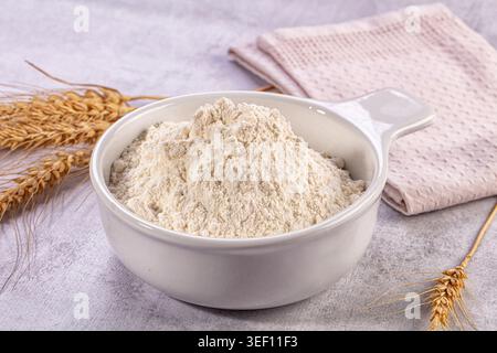 Close up still life image featuring ceramic bowl filled with fresh white flour, golden wheat stalks, folded light pink kitchen towel Stock Photo
