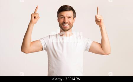Young Man Smiling and Pointing Upwards With Both Hands Indoors Stock Photo