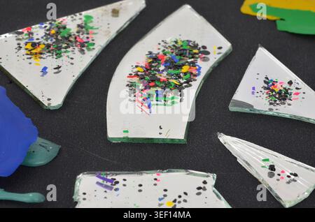 Tiny, colored pieces of plastic reflected in broken mirror on dark background. Shallow depth of field - garbage as an abstraction. Stock Photo