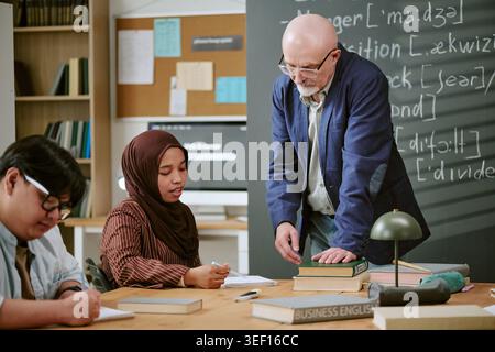 Senior Teacher Assisting Migrant Students during Classroom Lesson Stock Photo