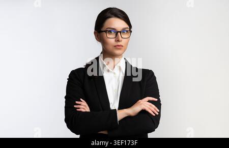 Confident Businesswoman Wearing Glasses Poses With Crossed Arms Against a Neutral Background Stock Photo
