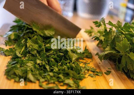 Slicing, cutting green parsley on a cutting board with a knife for cooking vegetarian food cook hands. Stock Photo