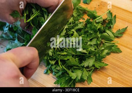 Slicing, cutting green parsley on a cutting board with a knife for cooking vegetarian food cook hands. Stock Photo