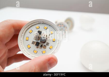 Man hand holding the broken white LED lamp, isolated on white background. Broken white led lamp circuits. Broken led light components. Stock Photo