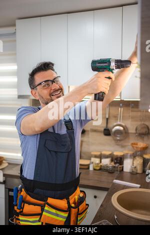Smiling handyman using cordless drill installing kitchen cabinets Stock Photo