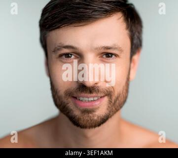 Young Man With Short Dark Hair and Beard Smiling at the Camera in a Neutral Background Stock Photo