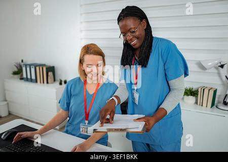Two nurses are discussing patient records and using a computer in a clinical setting Stock Photo