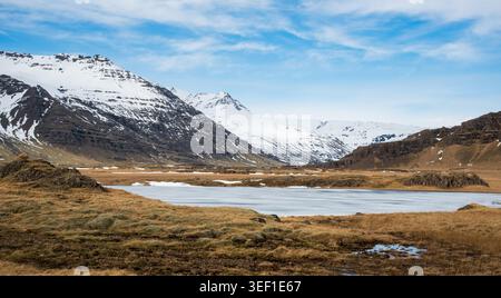 A wide view of mountains with snow in the background and a frozen lake in the valley. Icelandic spring landscape, Iceland Stock Photo