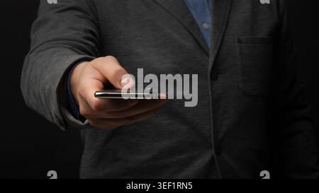 Business Professional Presenting Smartphone in Formal Attire Against Dark Background Stock Photo