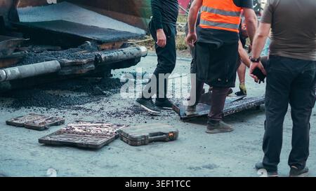 Road workers using heavy machinery and tools to lay fresh asphalt. Stock Photo